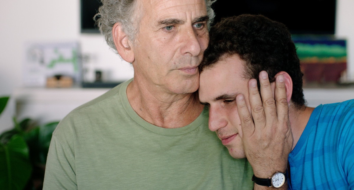 体を寄せ合う父と自閉症スペクトラムの息子　チャップリンのイラストも　「旅立つ息子へ」場面写真