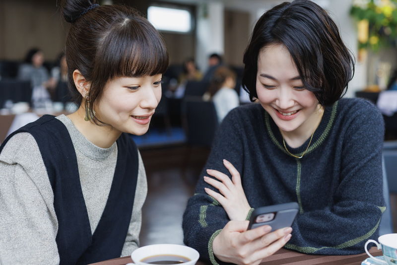 黒木華と藤間爽子がスマホを見ながら楽しそうに話す姿　心でつながる人々　「アイミタガイ」場面写真