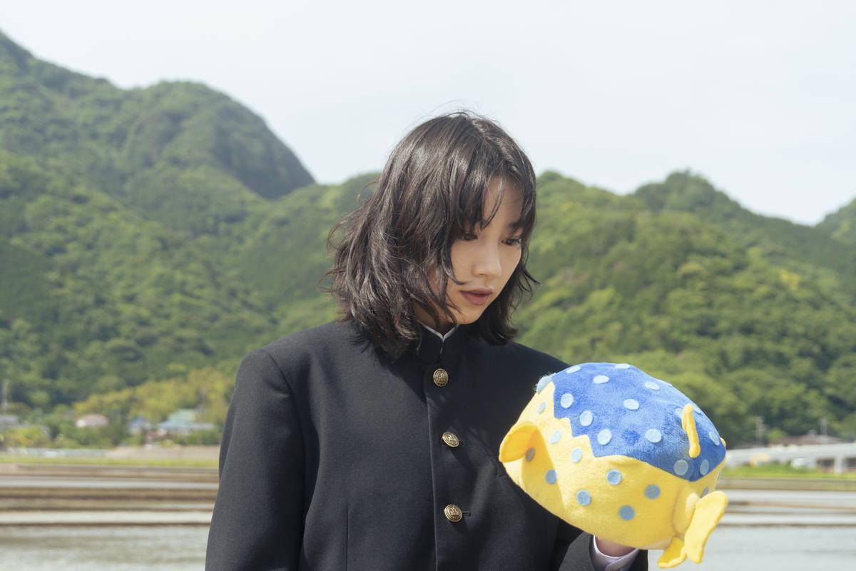 のん　頭にハコフグ帽子、たくさんの色鮮やかな魚の絵が描かれた服で笑顔　「さかなのこ」場面写真