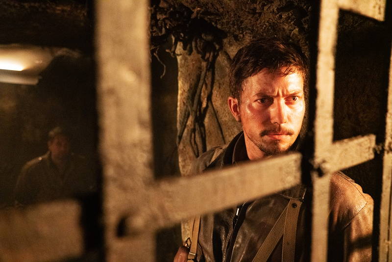 不気味な笑みを見せるミッキー・ローク　白骨死体を見つける兵士　「ウォーハント 魔界戦線」場面写真