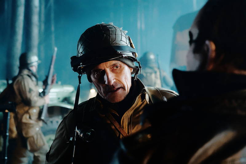 不気味な笑みを見せるミッキー・ローク　白骨死体を見つける兵士　「ウォーハント 魔界戦線」場面写真